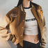 Person wearing a brown letterman jacket over a white crop top with visible branding.